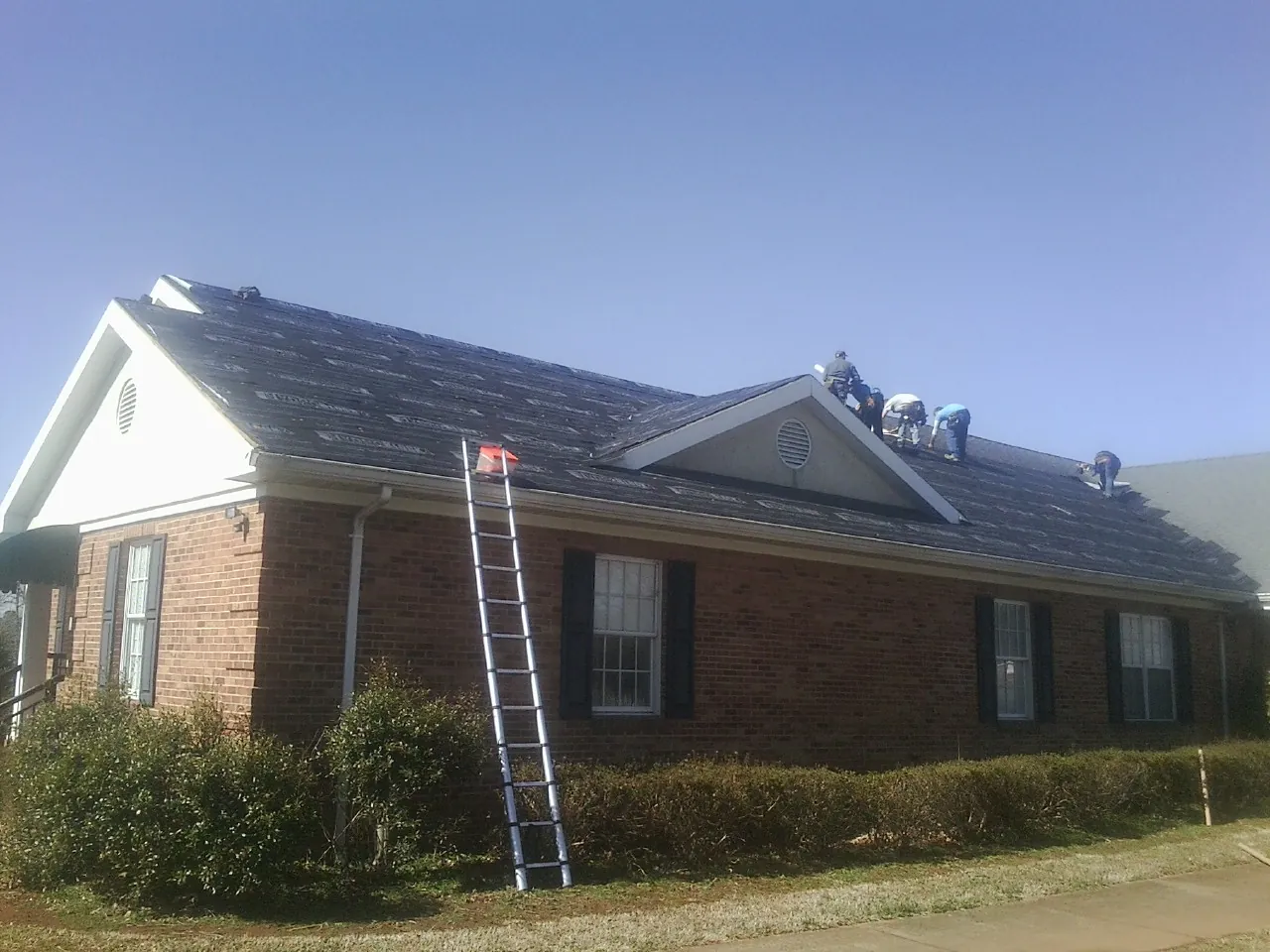 Crew tearing shingles off a brick ranch roof with a ladder set — Metal Roof Repair work by our crew in Port Orford