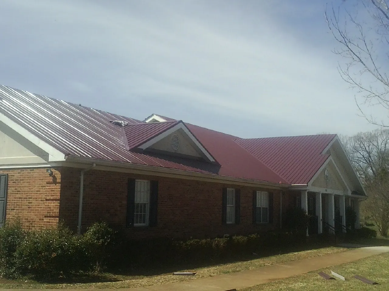 Red metal roof with gabled entries on a long brick building, from a Hail Damage Roof Repair job in Port Orford