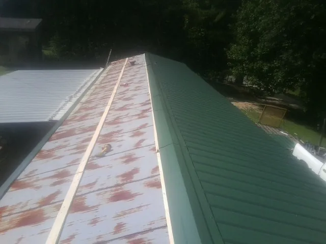 Old rusted panels beside newly installed green metal roofing — Wind Damage Roof Repair by Roofing Brothers in Port Orford