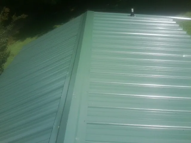 New green metal panels meeting at the ridge of a roof — Flat Roof Repair work by our crew in Port Orford