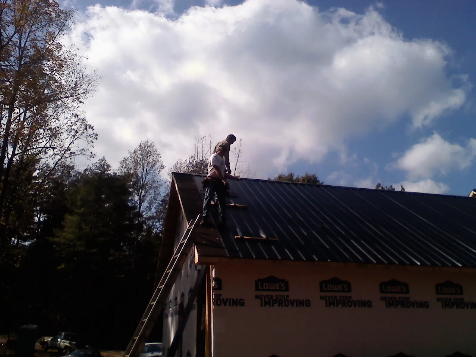 Roofer fastening dark metal panels high against a cloudy sky, from a Roof Inspection job in Port Orford