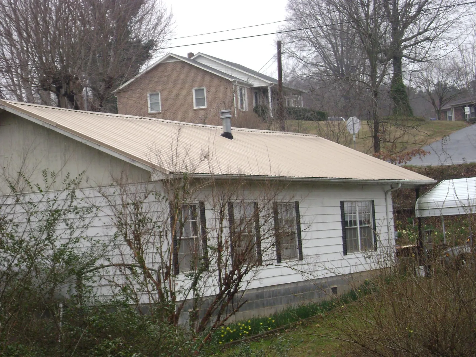 Tan metal roof on a white sided house set into a hillside — Commercial Roofing by Roofing Brothers in Port Orford